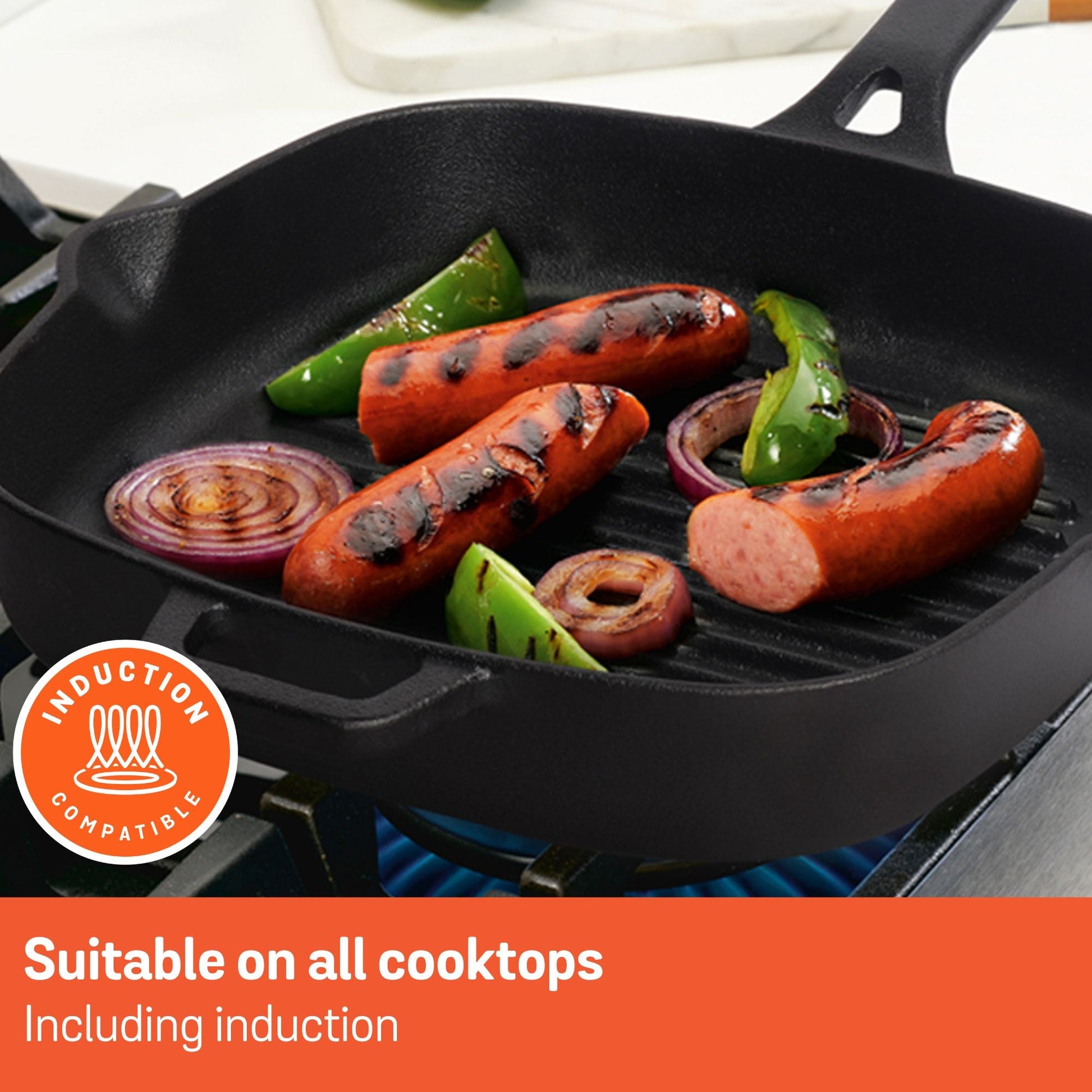Meyer cast iron grill pan with sausages, onions, and bell peppers cooking on a gas stovetop.